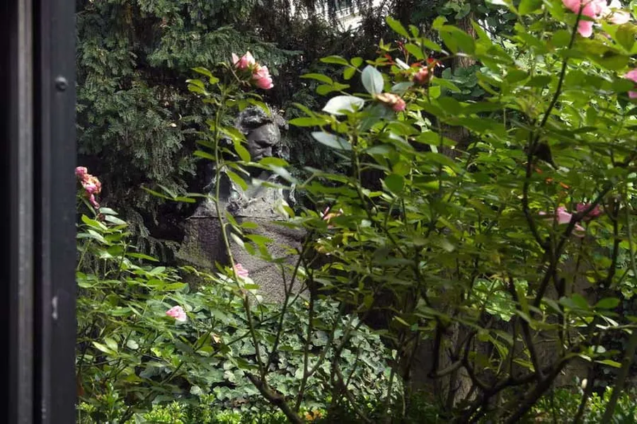 Blick aus dem Fenster des Kammermusiksaals in den romantischen Garten des Beethoven-Hauses. Zwischen Rosen hindurch sieht man die  große Bronzebüste, die den Komponisten nachdenklich und in sich gekehrt zeigt.